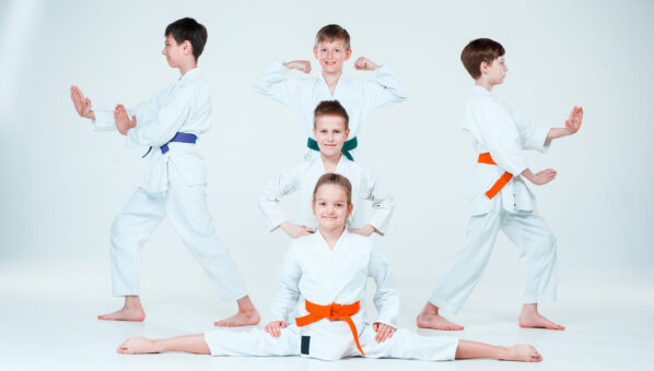 The teen boys and girl fighting at Aikido training in martial arts school. Healthy lifestyle and sports concept. Teenagers in white kimono on white background. Children with concentrated faces posing at studio